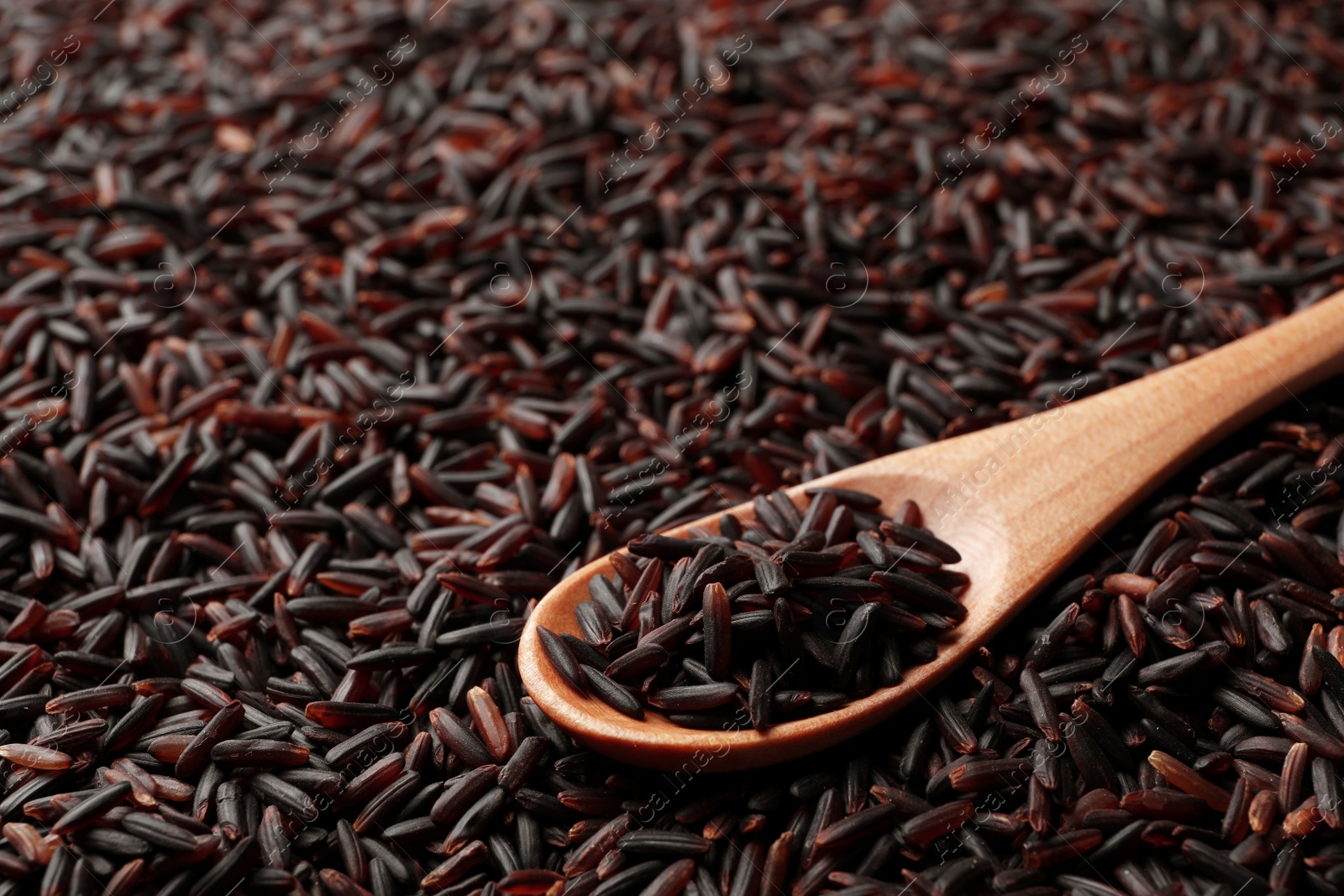 Photo of Wooden spoon with raw brown rice on cereal, closeup view