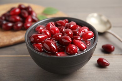 Photo of Delicious dogwood jam with berries in bowl on wooden table, closeup