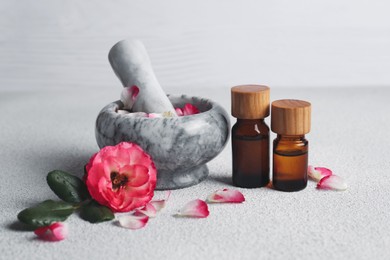 Photo of Glass bottles of aromatic essential oil, mortar with roses on white table