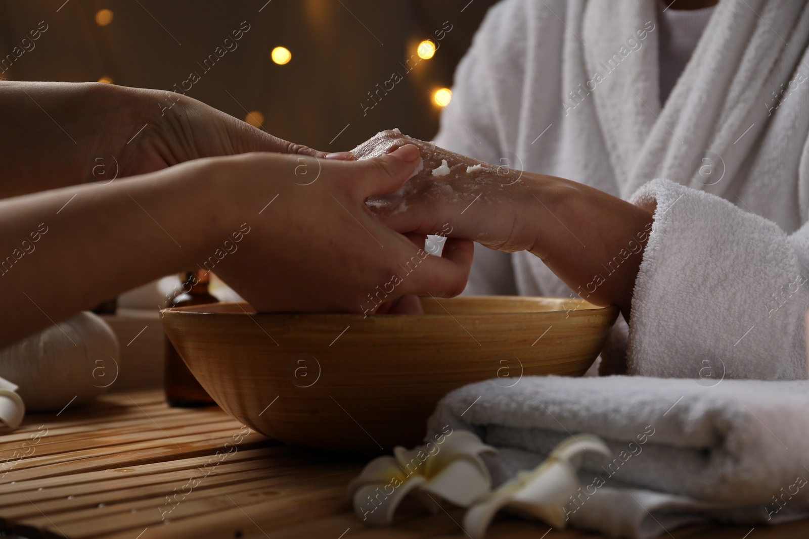 Photo of Woman receiving hand treatment at wooden table in spa, closeup