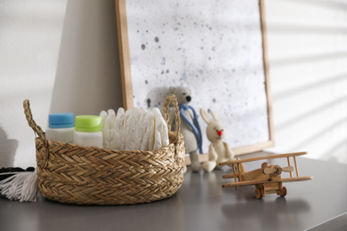 Photo of Wicker basket with accessories and wooden airplane on grey table in child room