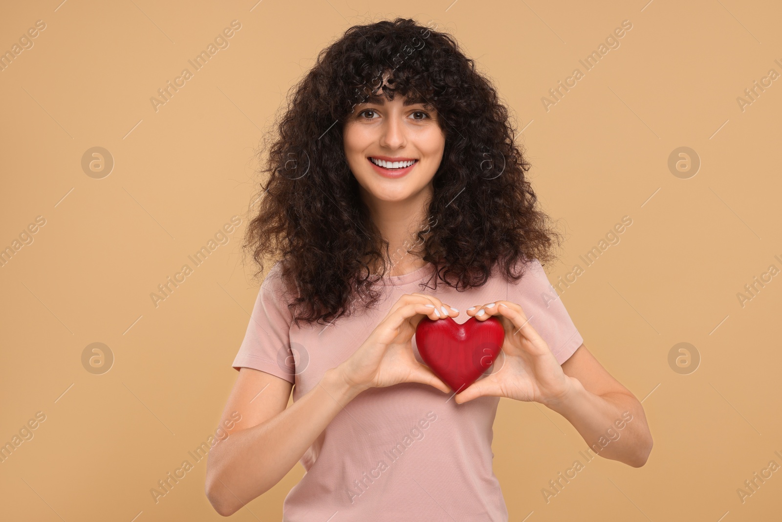 Photo of Happy young woman holding decorative red heart on beige background