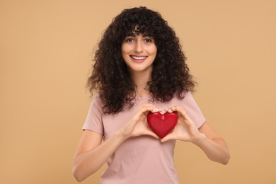 Happy young woman holding decorative red heart on beige background