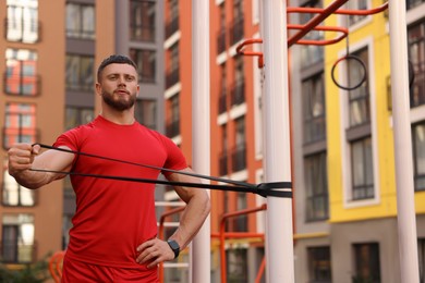 Muscular man doing exercise with elastic resistance band on sports ground