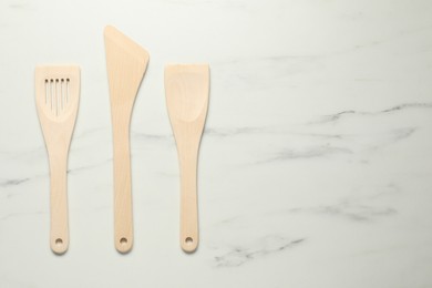 Photo of Different wooden spatulas on white marble table, flat lay. Space for text