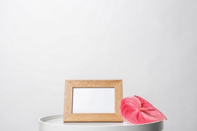 Photo of Blank frame and flower on table against white background. Mock up for design