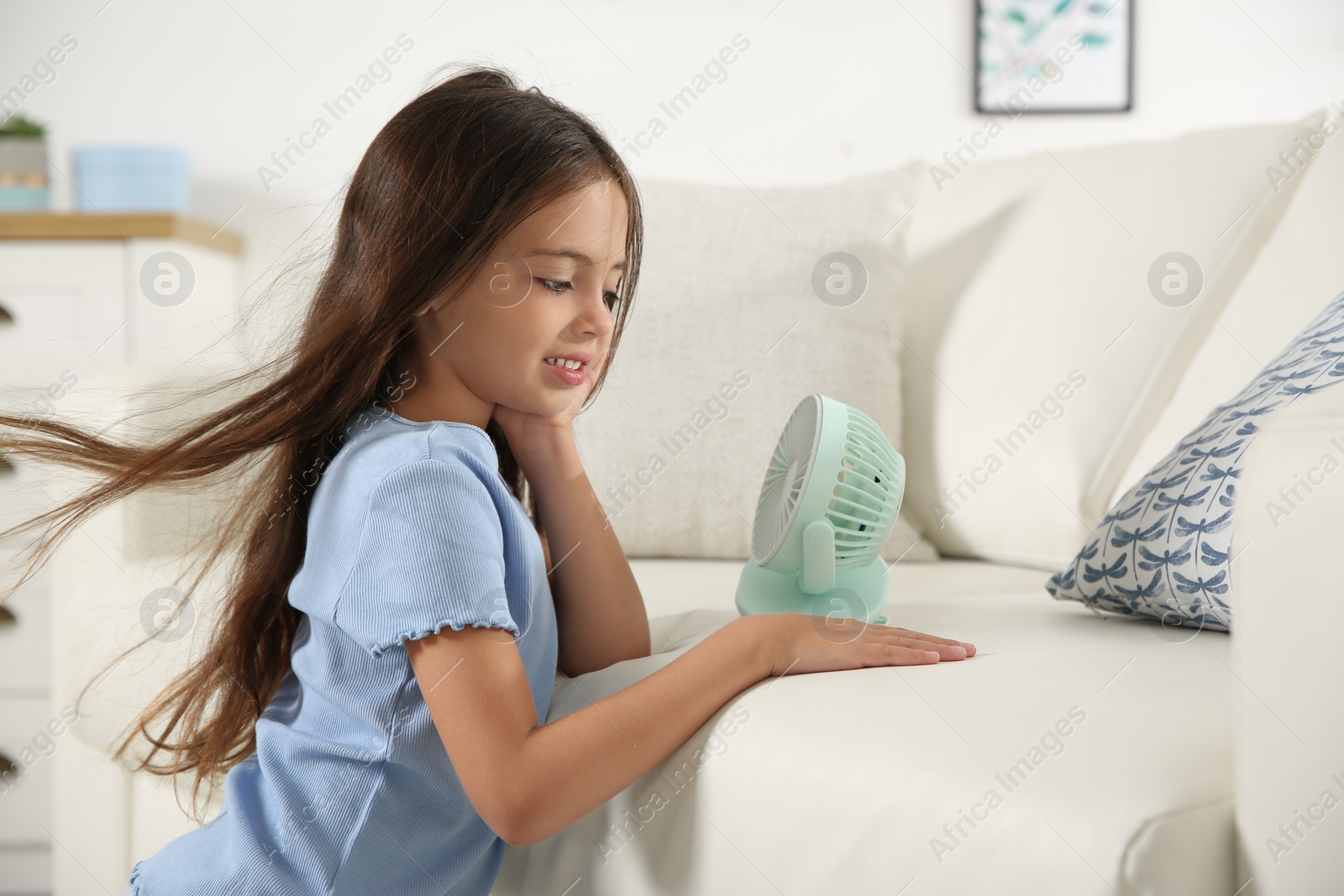 Photo of Little girl enjoying air flow from portable fan at home. Summer heat