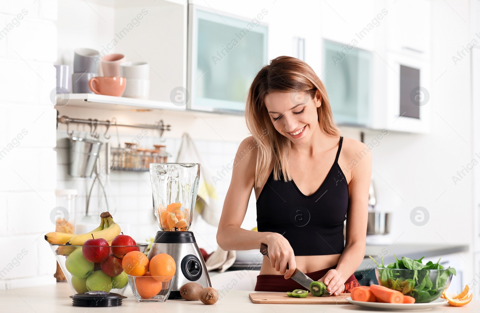 Photo of Young woman preparing tasty healthy smoothie at table in kitchen