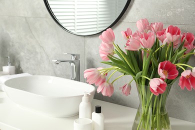 Photo of Vase with beautiful pink tulips and toiletries near sink in bathroom