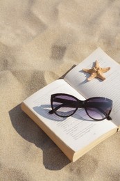 Photo of Beautiful sunglasses, book and starfish on sand. Space for text