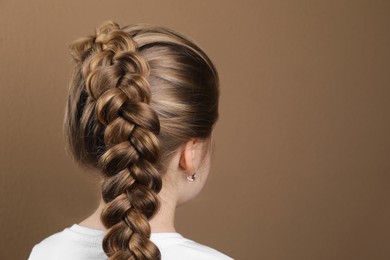Photo of Little girl with braided hair on light brown background, back view. Space for text