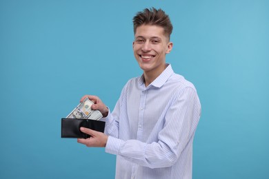 Photo of Happy man putting dollar banknotes into wallet on light blue background