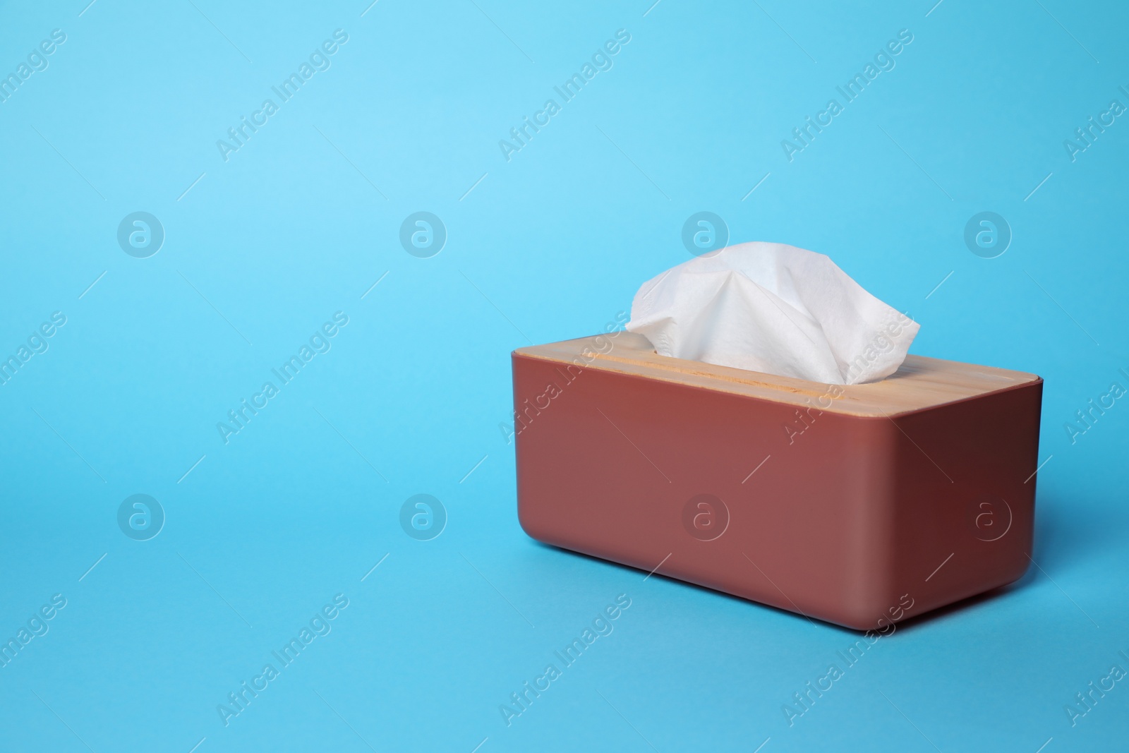 Photo of Holder with paper tissues on light blue background. Space for text