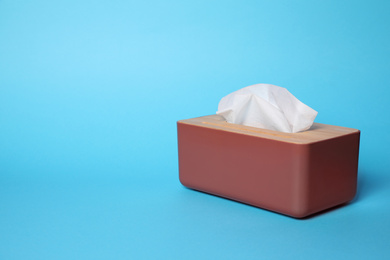 Photo of Holder with paper tissues on light blue background. Space for text