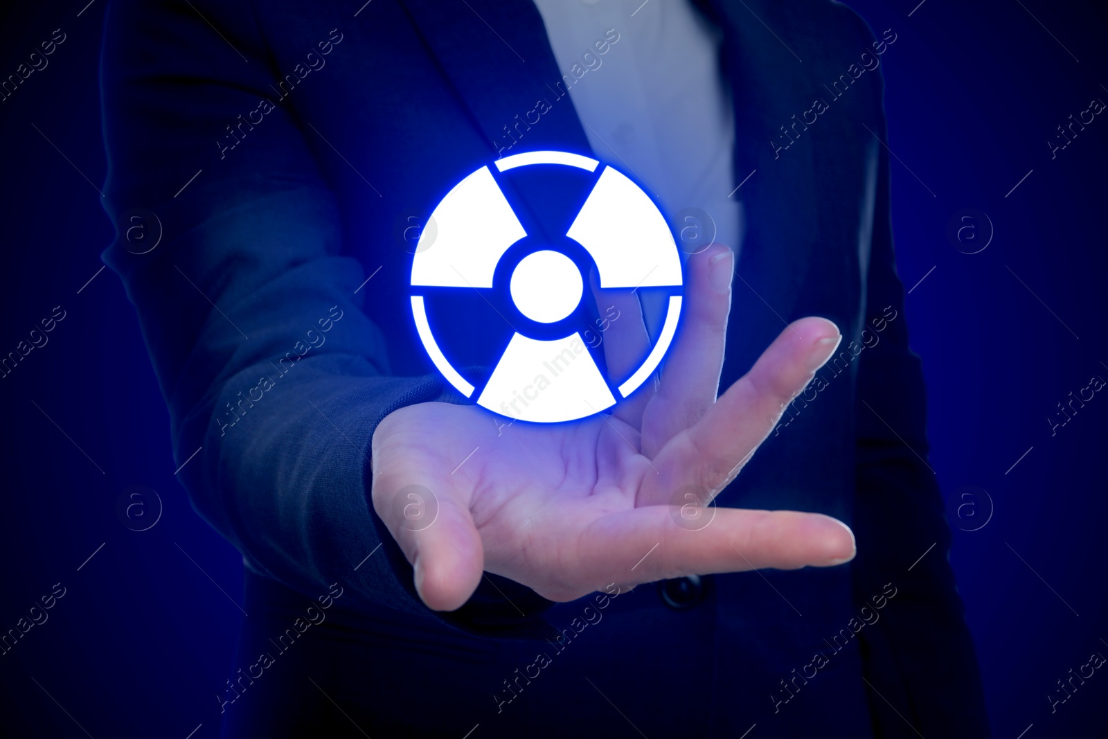 Image of Woman holding glowing radiation warning symbol on dark blue background, closeup