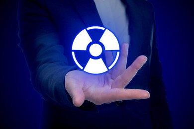 Image of Woman holding glowing radiation warning symbol on dark blue background, closeup