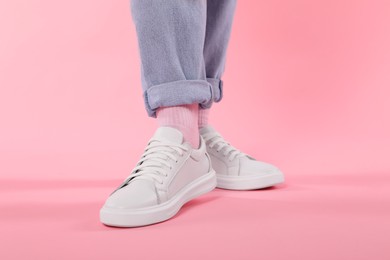 Photo of Woman wearing stylish white sneakers on pink background, closeup