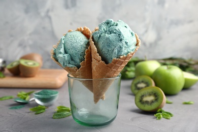 Photo of Composition with delicious spirulina ice cream cones in glass on table against grey background