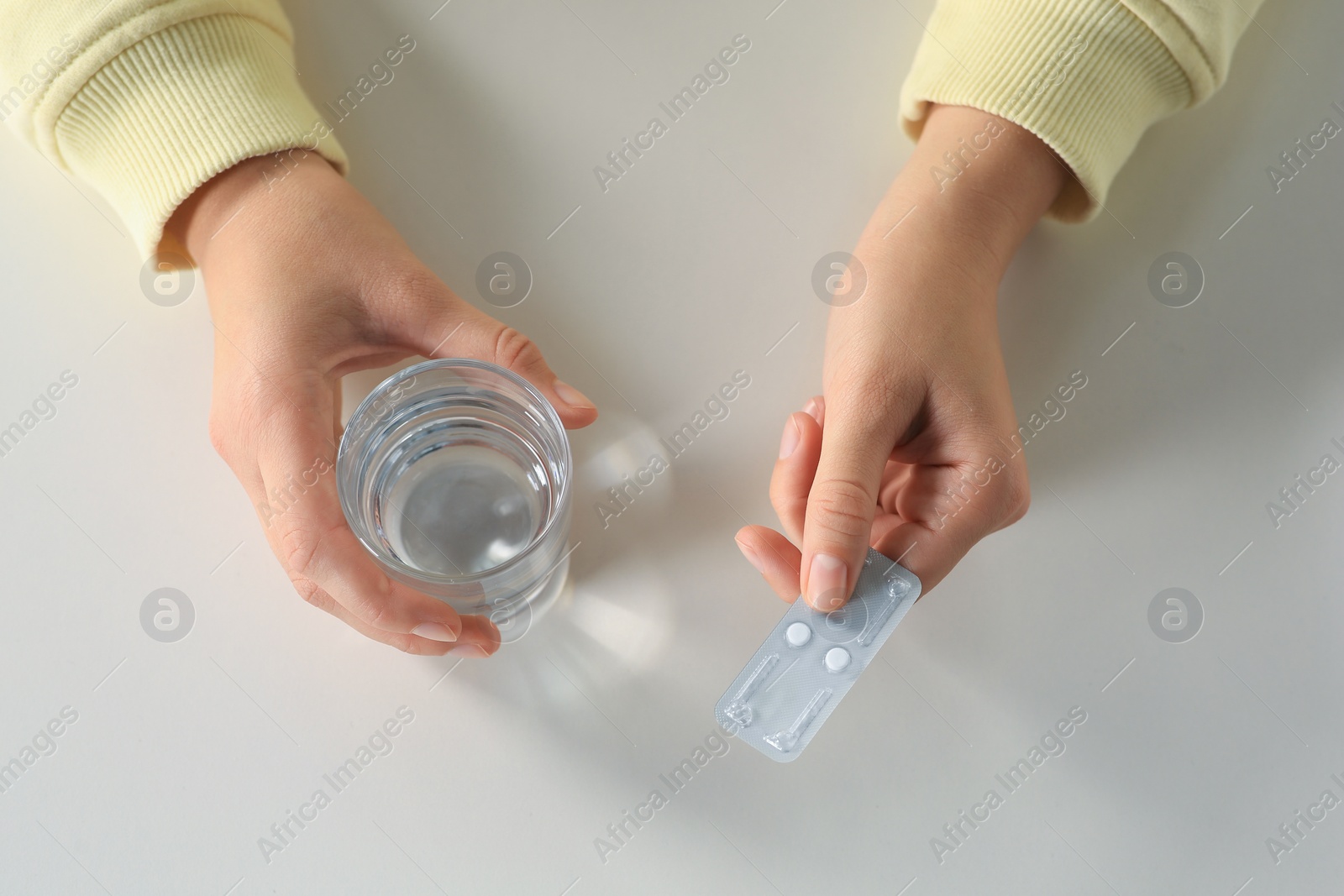 Photo of Woman taking emergency contraception pill at white table indoors, closeup