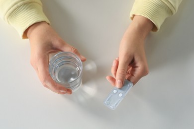 Woman taking emergency contraception pill at white table indoors, closeup