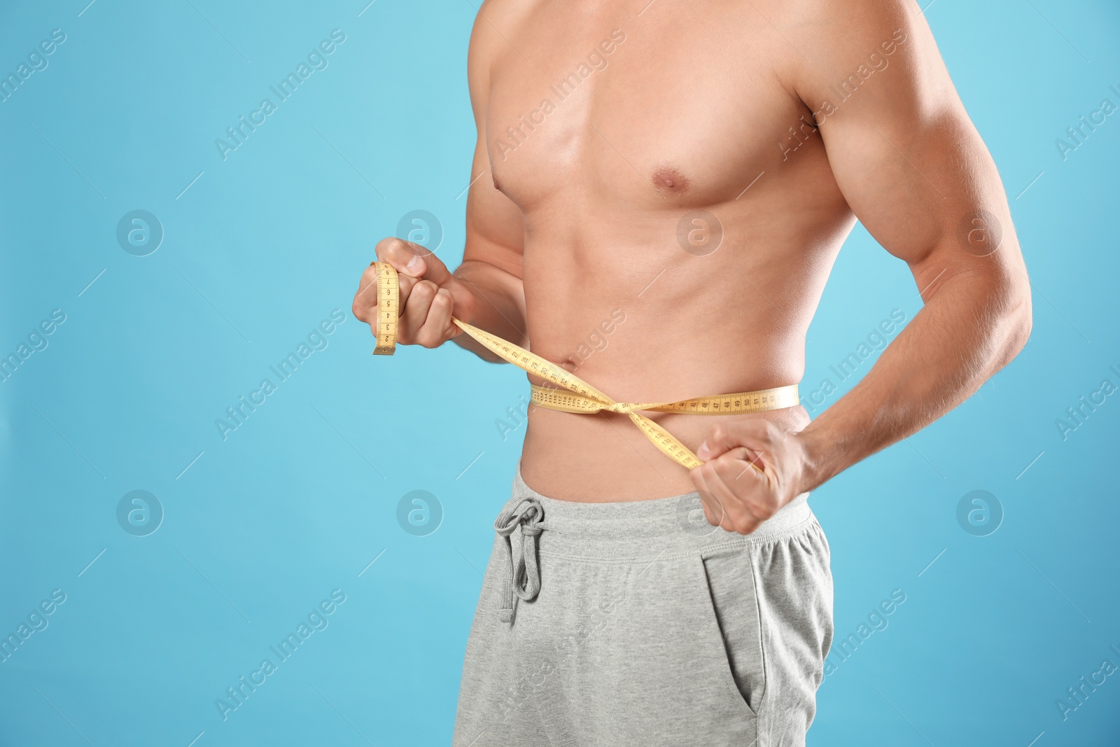 Photo of Young man with slim body using measuring tape on light blue background, closeup view. Space for text