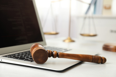 Photo of Laptop, wooden gavel and scales on white table, closeup. Cyber crime