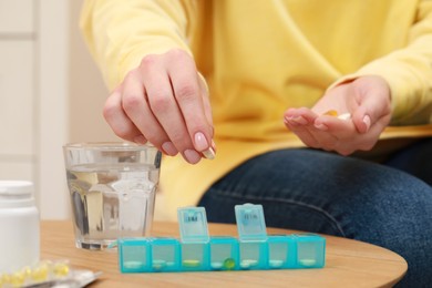 Photo of Woman taking pill from plastic box at wooden table indoors, closeup