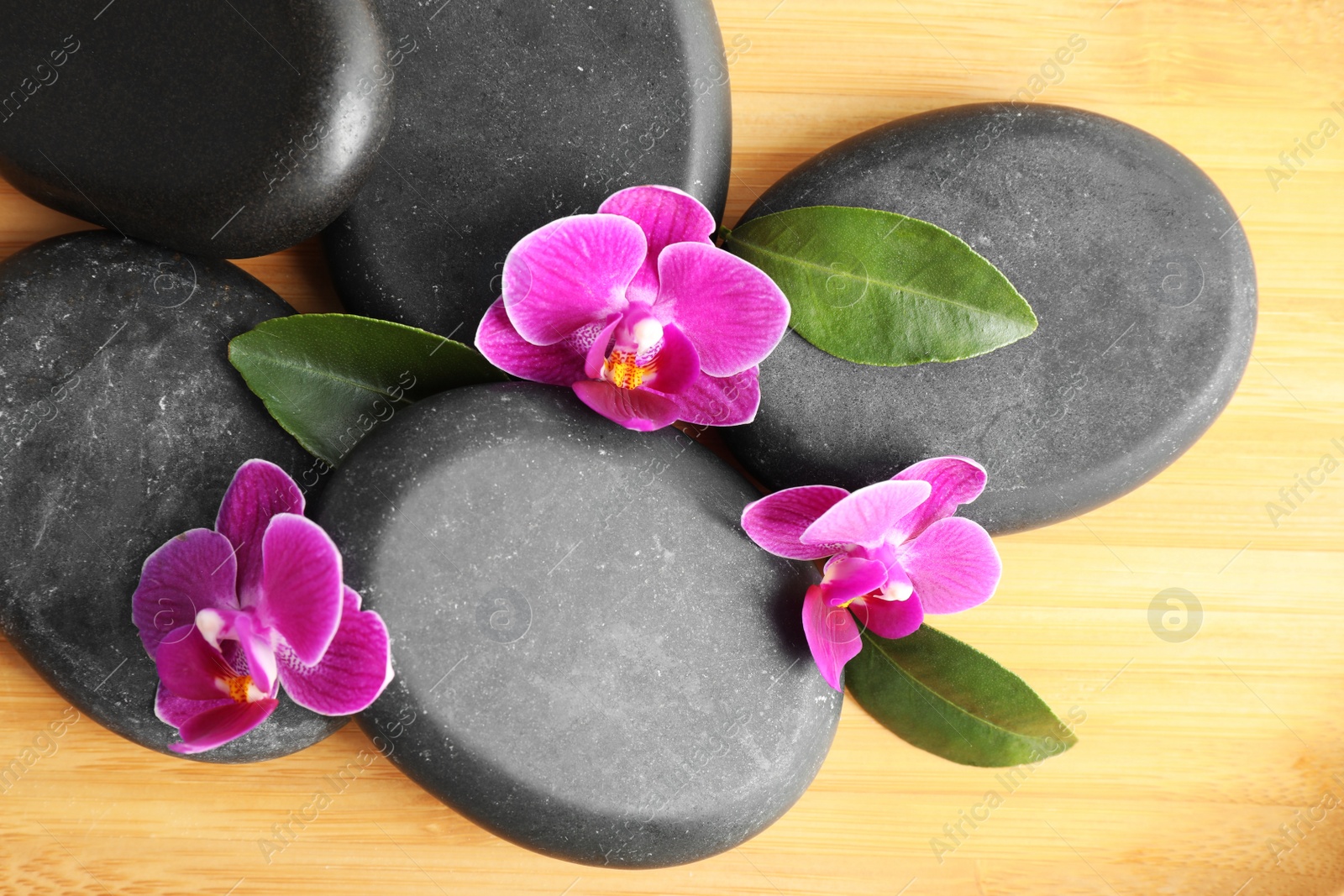 Photo of Spa stones and orchid flowers on wooden background, top view