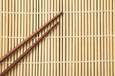 Photo of Pair of wooden chopsticks on bamboo mat, top view. Space for text