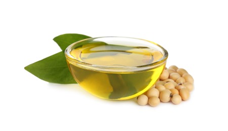 Glass bowl of oil, soybeans and leaves on white background