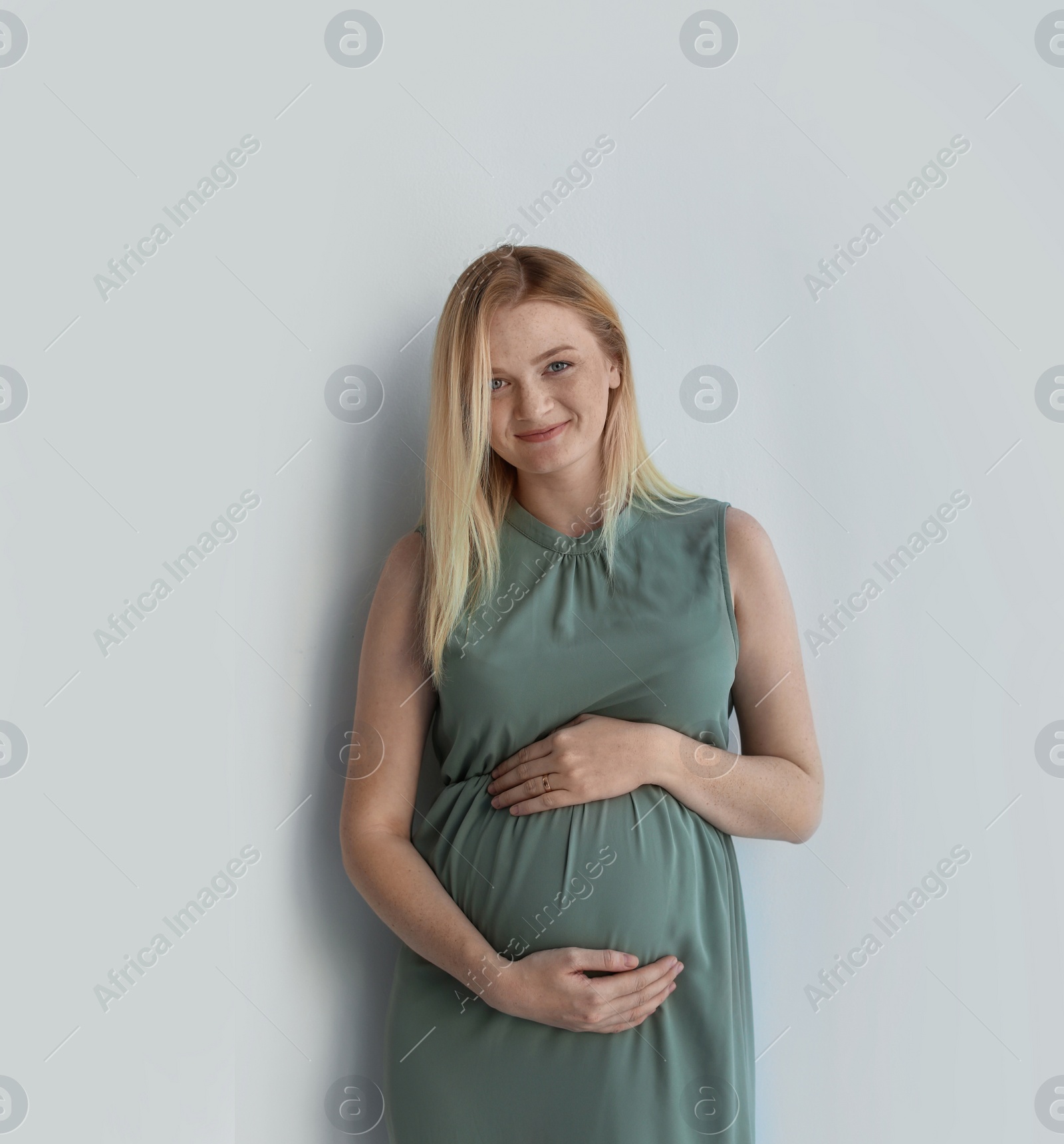 Photo of Young pregnant woman touching belly on light background