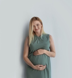 Young pregnant woman touching belly on light background