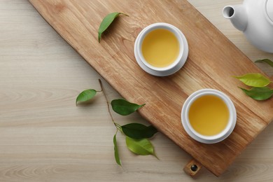 Tray with white cups of green tea, leaves and teapot on wooden table, flat lay. Space for text