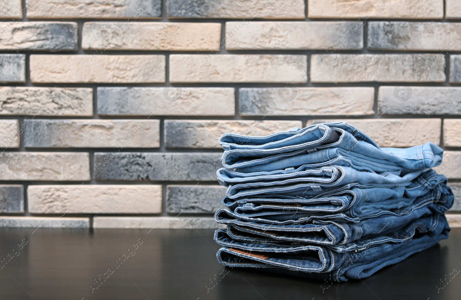 Photo of Stack of stylish jeans on table against brick wall