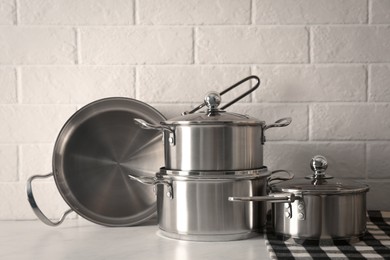 Set of stainless steel cookware on table near white brick wall