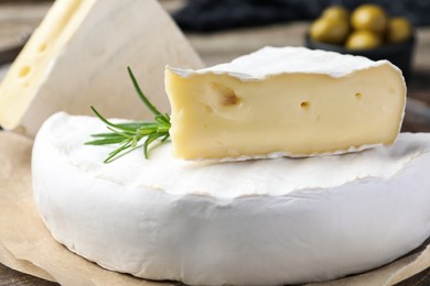 Photo of Tasty cut brie cheese with rosemary on parchment
