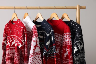 Different Christmas sweaters hanging on rack against light background