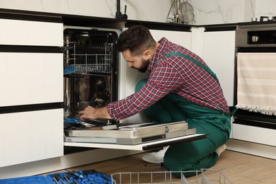 Serviceman repairing and examining dishwasher in kitchen