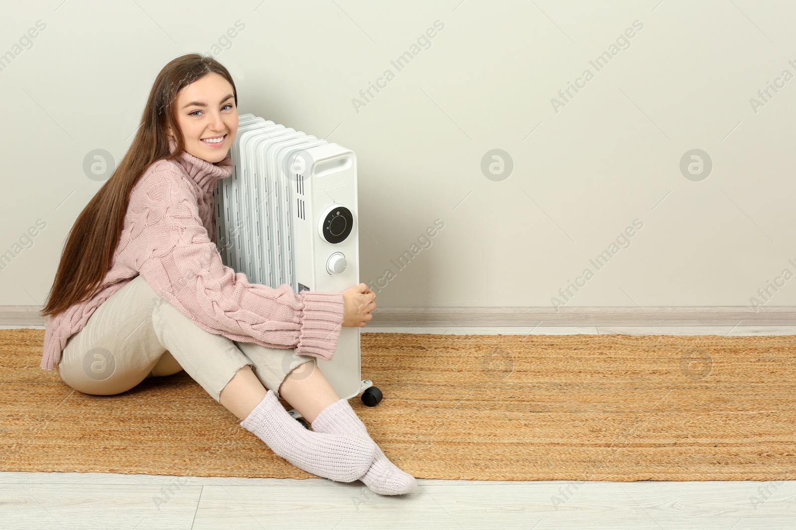 Photo of Young woman warming herself near modern electric heater indoors, space for text