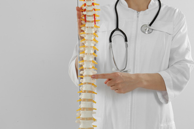 Photo of Female orthopedist with human spine model against light background, closeup