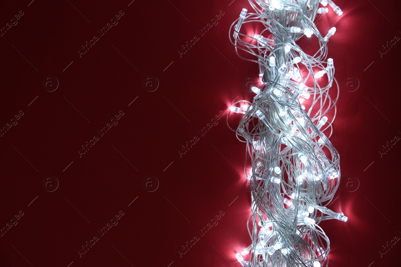 Photo of Glowing Christmas lights on burgundy background, top view. Space for text