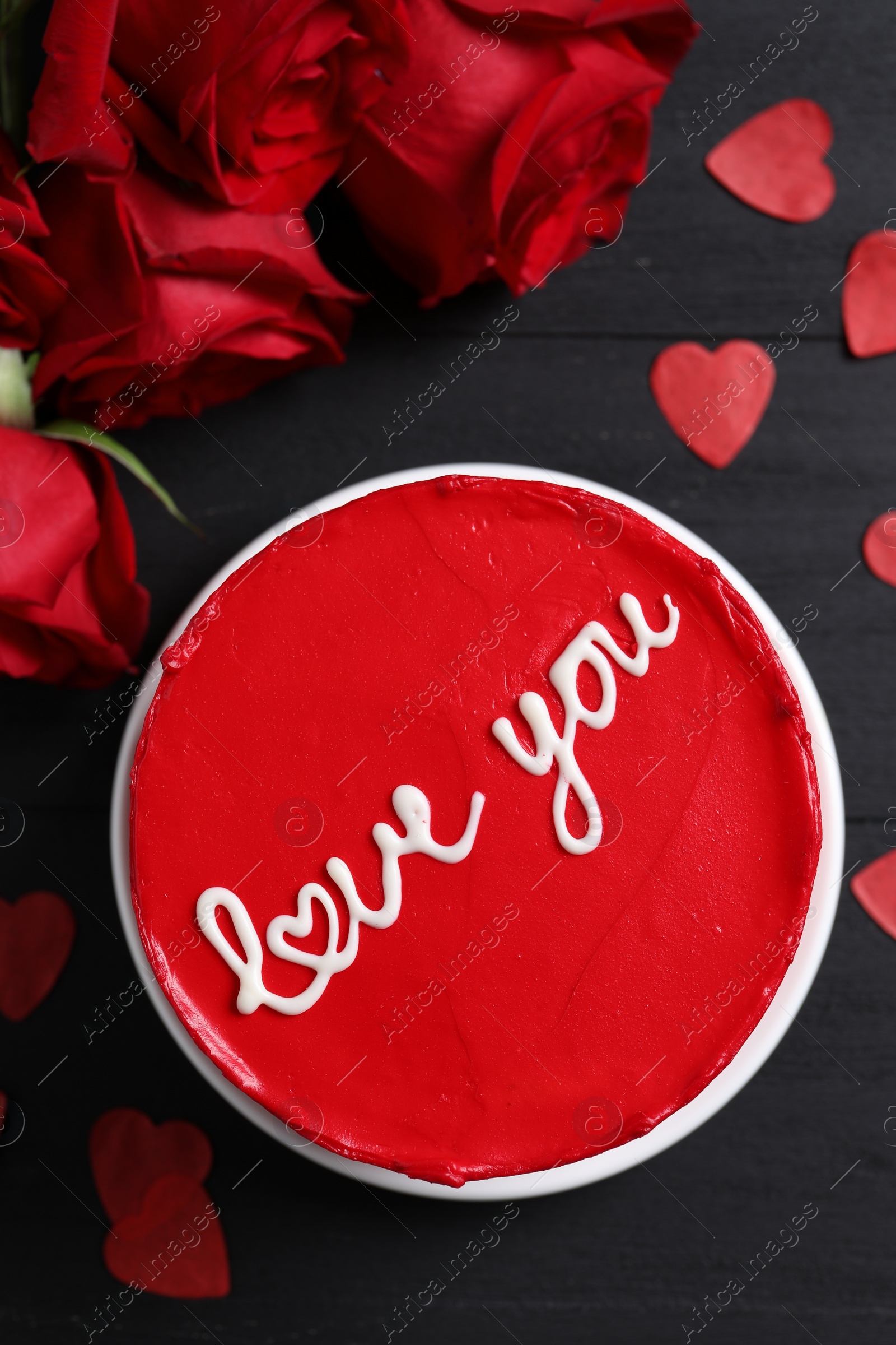 Photo of Bento cake with text Love You, roses and paper hearts on black wooden table, flat lay. St. Valentine's day surprise