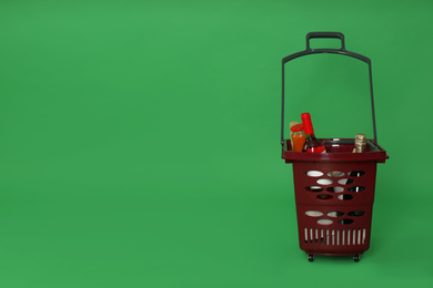 Photo of Shopping basket full of different products on green background. Space for text