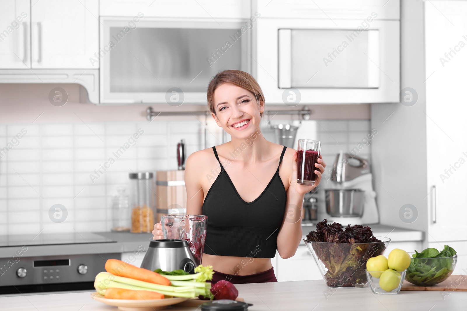 Photo of Young woman with glass of tasty healthy smoothie at table in kitchen