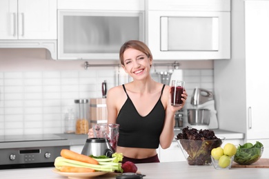 Photo of Young woman with glass of tasty healthy smoothie at table in kitchen