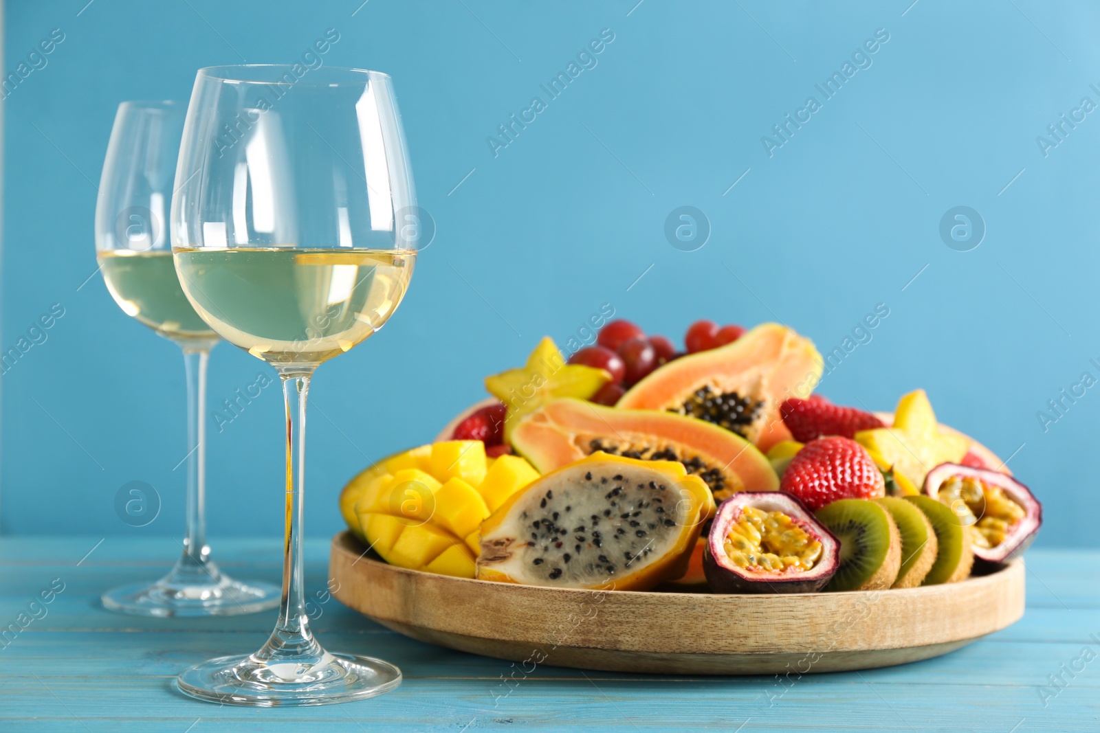 Photo of Delicious exotic fruits and glasses of wine on light blue wooden table