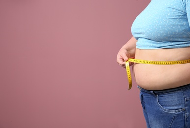 Photo of Overweight woman with measuring tape on color background