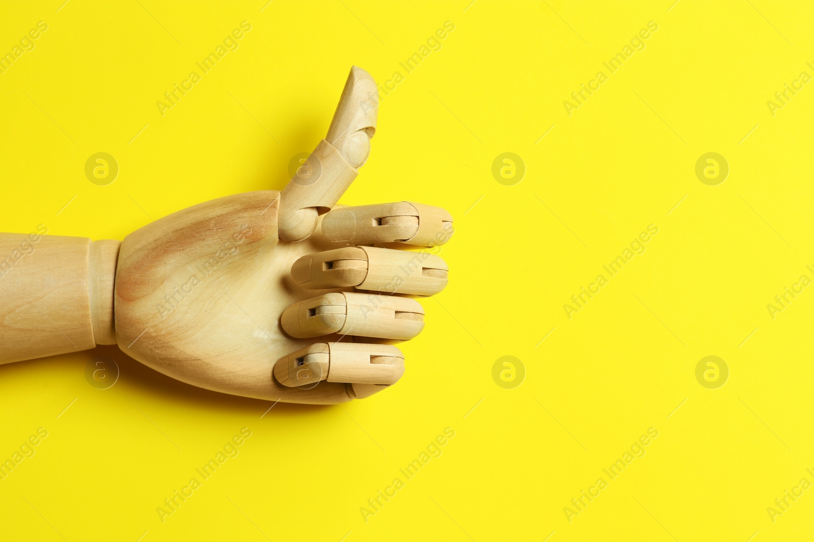 Photo of Wooden mannequin hand showing thumb up on yellow background, top view. Space for text