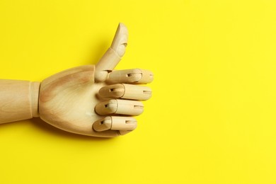 Wooden mannequin hand showing thumb up on yellow background, top view. Space for text