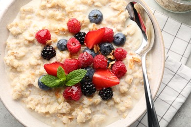 Bowl of oatmeal porridge served with berries on light grey table, top view